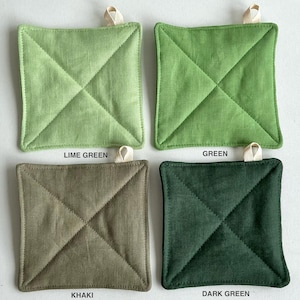 Puede incluir: Cuatro salvamanteles cuadrados acolchados en tonos verdes y caqui. Cada salvamanteles tiene un lazo para colgar. Los colores incluyen verde lima, verde, caqui y verde oscuro. El texto etiqueta cada color.