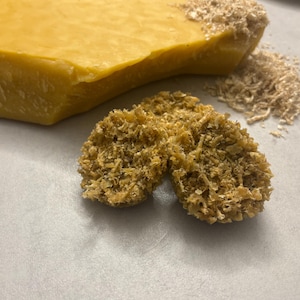 Könnte beinhalten: Nahaufnahme von gelbem Bienenwachs, mit einem Block und Spänen sowie zwei kleinen strukturierten Wachsformen. Das Wachs hat ein natürliches, organisches Aussehen, was auf ein handgefertigtes oder natürliches Produkt hindeutet. Das Bild ist gut beleuchtet.