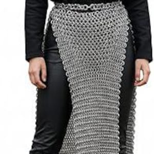 May include: A silver chainmail skirt featuring a linked metal ring construction with a waist chain belt. The skirt is worn over black trousers, paired with a black long-sleeved shirt and dark brown lace-up boots reaching mid-calf.