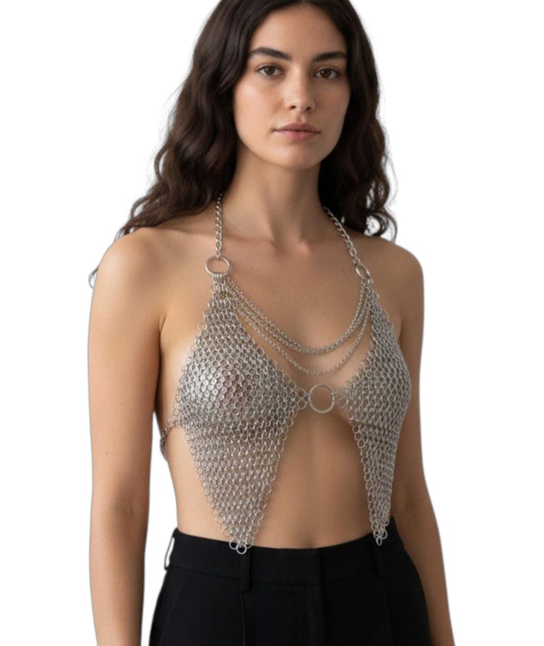 Puede incluir: Top halter de cota de malla plateada con dise&ntilde;o triangular. El top presenta m&uacute;ltiples hilos de cadena y detalles circulares. La prenda est&aacute; hecha de peque&ntilde;os anillos met&aacute;licos entrelazados.