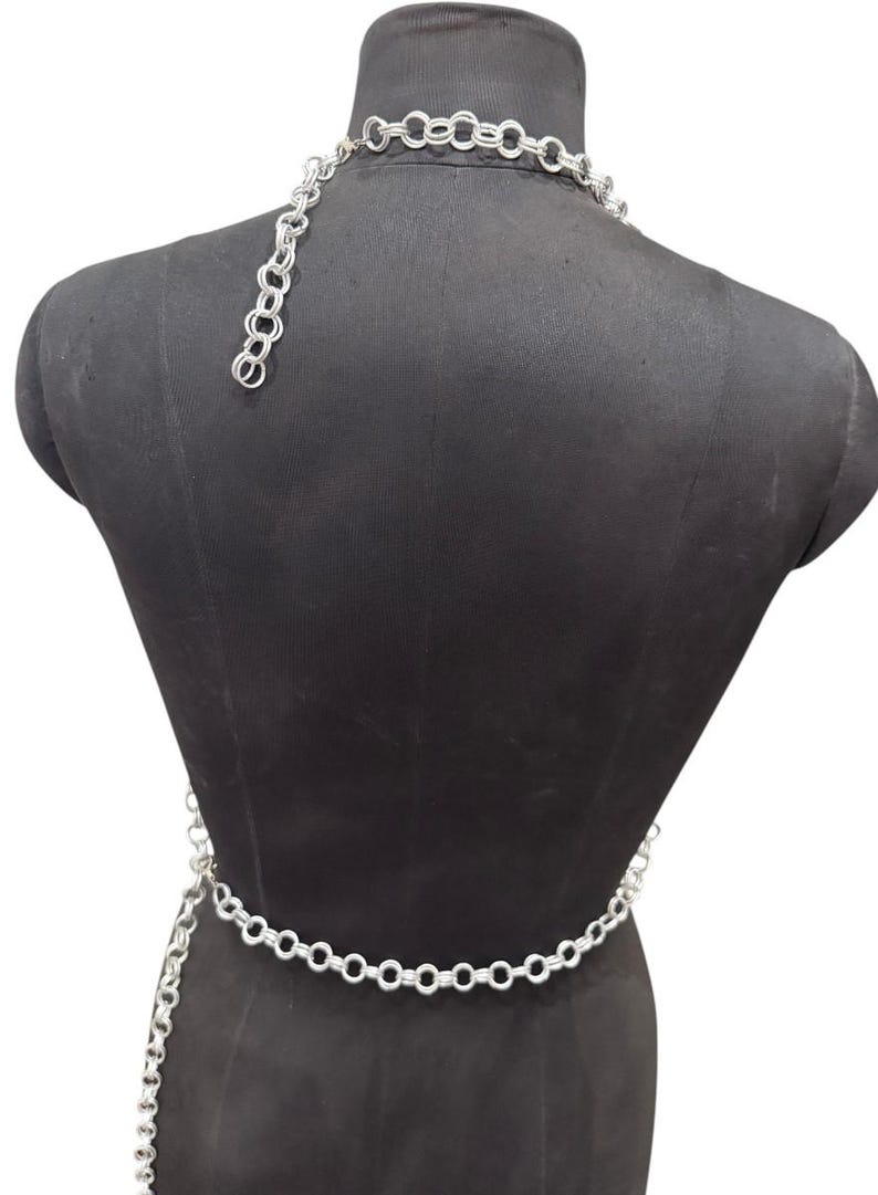 Puede incluir: Conjunto de cintur&oacute;n y collar de cadena plateada. El collar es de estilo gargantilla y el cintur&oacute;n est&aacute; dise&ntilde;ado para llevarse alrededor de la cintura. Las cadenas est&aacute;n hechas de eslabones circulares conectados. El conjunto se muestra en un maniqu&iacute; negro.