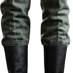 Könnte beinhalten: Graue Wollhose mit strukturierter Oberfläche kombiniert mit schwarzen, wadenhohen Lederstiefeln. Die Hose weist eine sichtbare Bügelfalte an der Vorderseite jedes Beins auf und der Text ZEMBORL ist diagonal auf den oberen Stoffbereich gedruckt.