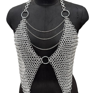 Puede incluir: Top de cota de malla plateada con dise&ntilde;o de cuello halter. La parte superior presenta una serie de anillos met&aacute;licos conectados que forman un patr&oacute;n similar a una malla. El dise&ntilde;o incluye anillos grandes en los hombros y un anillo central en la cintura, con cadenas delicadas.