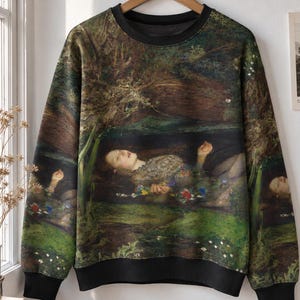 Op de afbeelding: Een sweatshirt met lange mouwen en ronde hals voorzien van een full-colour print van het schilderij Ophelia van John Everett Millais. Het kledingstuk heeft een effen zwarte geribbelde kraag, boorden en zoom die contrasteren met de print.