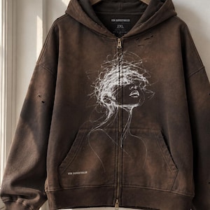 Può includere: Una felpa con cappuccio e zip marrone con finitura usurata e piccoli fori. Il davanti presenta un disegno a linee bianche di un volto con capelli spettinati. Il testo VON BURGSTHALER è stampato vicino all'orlo e sull'etichetta interna 2XL.
