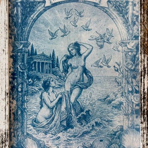 Puede incluir: Impresión enmarcada en azul y blanco que representa a Afrodita y Peitho, con palomas, arquitectura clásica y figuras en una escena costera. La obra de arte presenta un trabajo de línea detallado y está enmarcada en un marco de madera blanca desgastada.