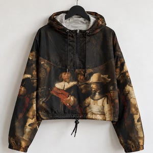 Könnte beinhalten: Ein schwarzer Langarm-Kapuzenpullover mit einem Druck der Nachtwache von Rembrandt. Das Kleidungsstück verfügt über einen halben Reißverschluss vorne, eine Kapuze mit Kordelzug und einen verstellbaren Saum mit schwarzen Kordelstoppern.