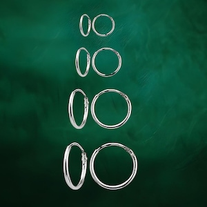 May include: A collection of silver hoop earrings of varying sizes are displayed against a dark green background. The earrings are round and shiny, reflecting light. The image showcases the different sizes available, from small to larger hoops, highlighting the jewelry's simple design.