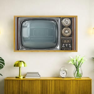 Puede incluir: Un televisor antiguo con marco de madera está montado en una pared blanca. El televisor tiene una pantalla plateada y un panel de control con perillas y diales. Debajo del televisor hay un mueble amarillo con una lámpara, libros y un reloj.