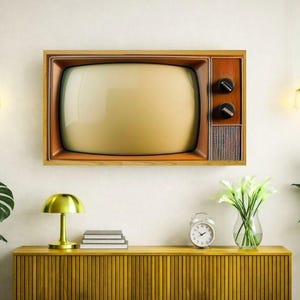 Puede incluir: Un televisor vintage con marco de madera está montado en una pared blanca. El televisor tiene una pantalla color crema y perillas negras. Una lámpara dorada, libros y un jarrón con flores se encuentran en un mueble de madera.