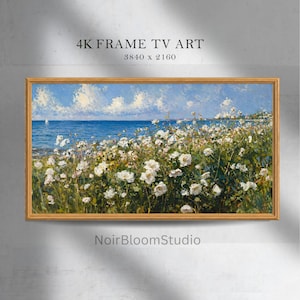Puede incluir: Una pintura de paisaje enmarcada representa una escena costera con flores blancas en primer plano, un mar azul y un cielo brillante. La obra de arte está etiquetada como "4K FRAME TV ART" y "NoirBloomStudio".