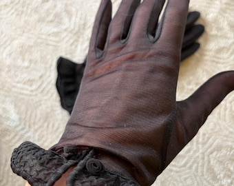 May include: A pair of sheer black gloves. The gloves are made of a delicate, see-through fabric. The wrist of each glove is adorned with a decorative, ruffled trim. The gloves are likely vintage or designed to evoke a vintage aesthetic.