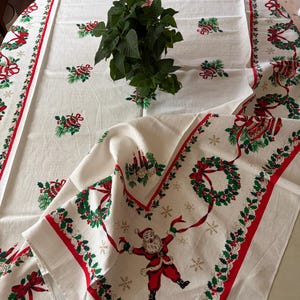 Peut inclure: Une nappe blanc cassé ornée d'un motif de fête avec des couronnes de houx rouges et vertes, des cloches et une figure centrale du Père Noël. La bordure est décorée de rubans rouges et de feuillage vert, agrémentée de petits flocons dorés.