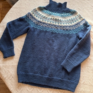 Könnte beinhalten: Ein blauer Strickpullover mit hohem, gerüschtem Kragen. Der Einsatz hat ein detailliertes Muster in Weiß, Blau und Grau. Die langen Ärmel und der Körper sind einfarbig tiefblau. Dieser Pullover ist ideal für kaltes Wetter.