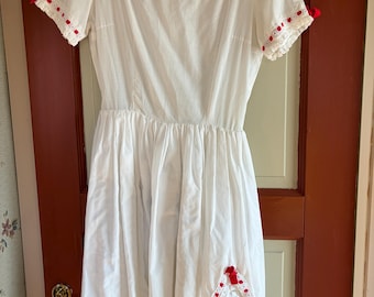 May include: A white dress with a square neckline and short sleeves. The neckline and sleeves are trimmed with red polka dots and lace. Red bows accent the sleeves. A white, ruffled embellishment with red trim is on the skirt.