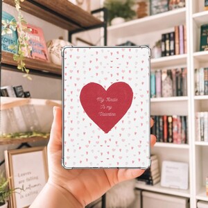 Könnte beinhalten: Eine transparente Kindle-Hülle mit Valentinstags-Design. Sie zeigt ein großes rotes Herz mit dem Text "My Kindle is my Valentine" und kleine rosa Herzen auf weißem Hintergrund.