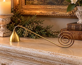 May include: A gold-toned metal candle snuffer featuring a long, slender handle that curves into a decorative spiral at one end and a bell-shaped extinguisher at the other, designed for safely putting out candle flames.