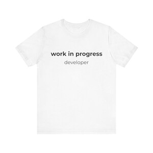 May include: White t-shirt with the text "work in progress" above "developer" in black, sans-serif font. The shirt is plain and has short sleeves.