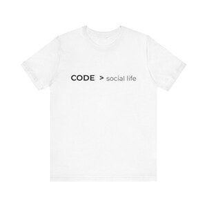 Op de afbeelding: Wit T-shirt met de tekst "CODE > social life" in zwart. Het shirt heeft korte mouwen en een ronde hals. De tekst is centraal op de borst gedrukt. Het T-shirt is gemaakt van zacht materiaal.