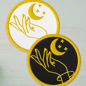 May include: Two embroidered patches. One features a white background with a gold outline, a gold hand, crescent moon, and stars. The other patch has a black background with the same design. Both patches have a gold border.