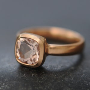 May include: A rose gold ring with a square-shaped, light pink gemstone.