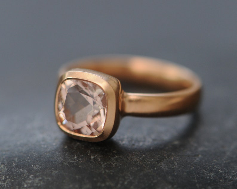 May include: A rose gold ring with a square-shaped, light pink gemstone.