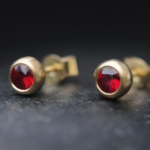 May include: A pair of gold stud earrings with red gemstones.