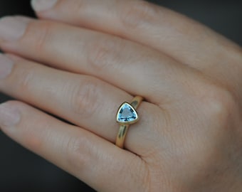 May include: A gold ring with a triangular blue gemstone set in the center.