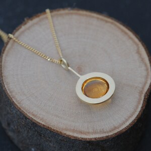 May include: A gold necklace with a pendant featuring a round, amber-colored stone set in a gold frame.