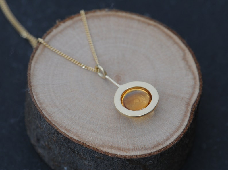 May include: A gold necklace with a pendant featuring a round, amber-colored stone set in a gold frame.