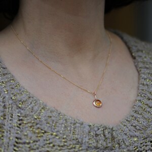 May include: A gold chain necklace with a small round pendant featuring a yellow gemstone.