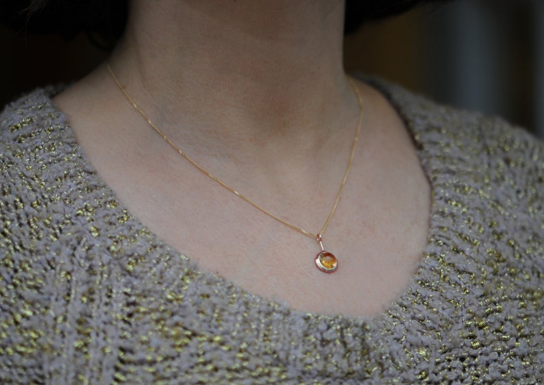 May include: A gold chain necklace with a small round pendant featuring a yellow gemstone.