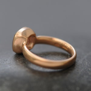 May include: A rose gold ring with a bezel set gemstone. The ring is simple and elegant.
