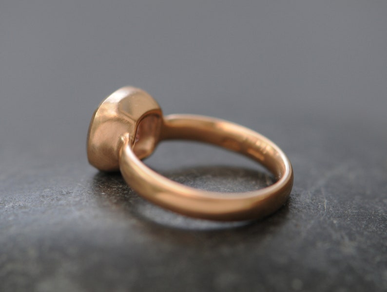 May include: A rose gold ring with a bezel set gemstone. The ring is simple and elegant.