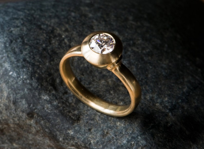 May include: A gold ring with a round, bezel-set diamond.