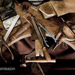 May include: A wooden workbench with various tools and supplies for jewelry making, including pliers, a hammer, a ruler, a file, and a small box of tools. The workbench is covered in a brown leather surface.