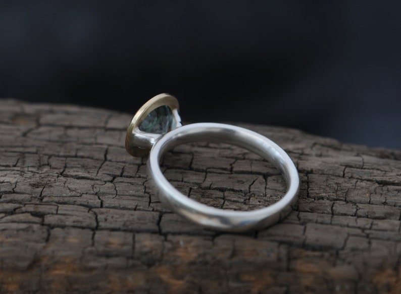 Puede incluir: Un anillo de plata con engaste de oro y una piedra preciosa verde.