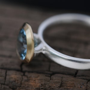 Puede incluir: Un anillo de plata con una piedra preciosa azul engastada en un engaste de oro.