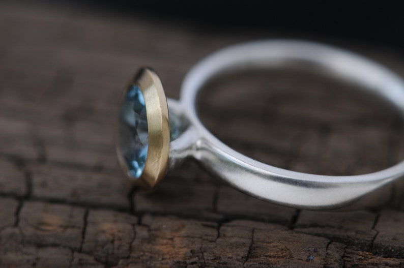 Puede incluir: Un anillo de plata con una piedra preciosa azul engastada en un engaste de oro.