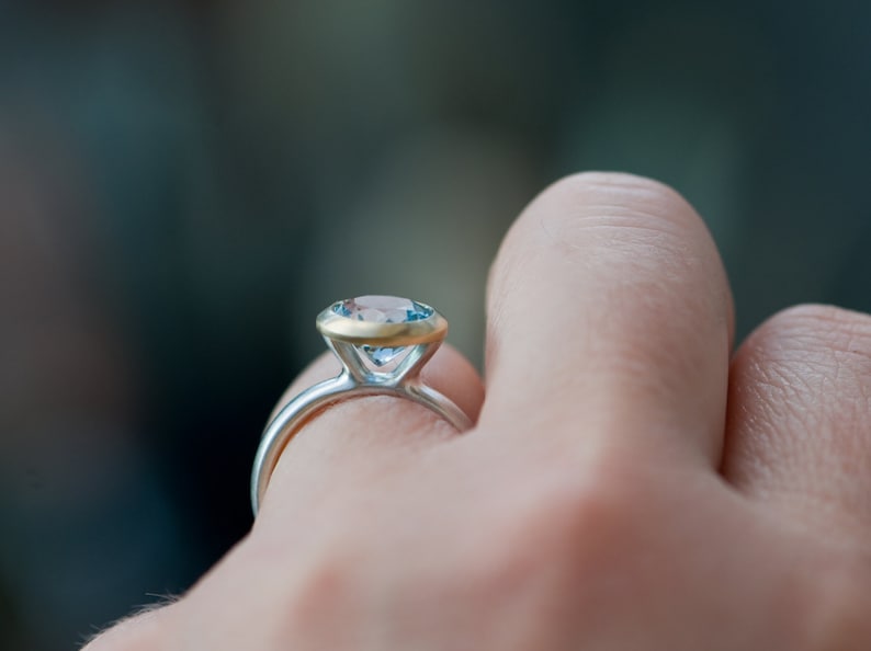 Puede incluir: Un anillo de plata con una banda de oro y una piedra preciosa azul.