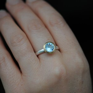 Puede incluir: Un anillo de plata con un engaste de oro y una piedra preciosa azul claro.