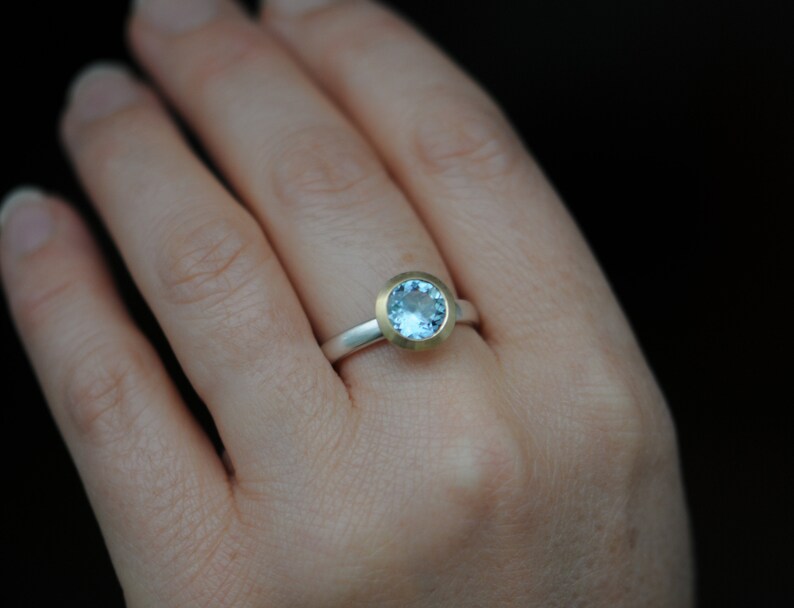 Puede incluir: Un anillo de plata con un engaste de oro y una piedra preciosa azul claro.