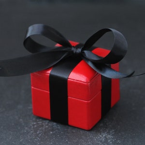 May include: A red gift box with a black ribbon. The box is tied with a bow and the ribbon is wrapped around the box.