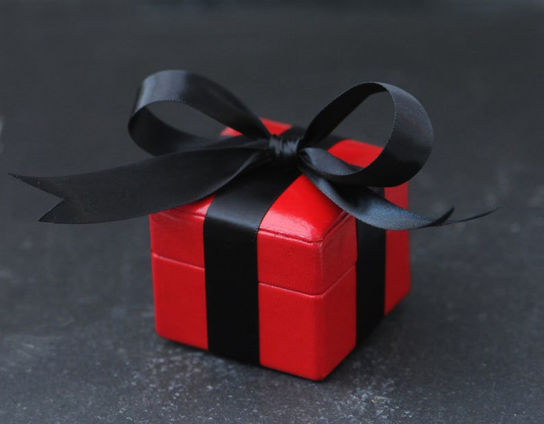 May include: A red gift box with a black ribbon. The box is tied with a bow and the ribbon is wrapped around the box.