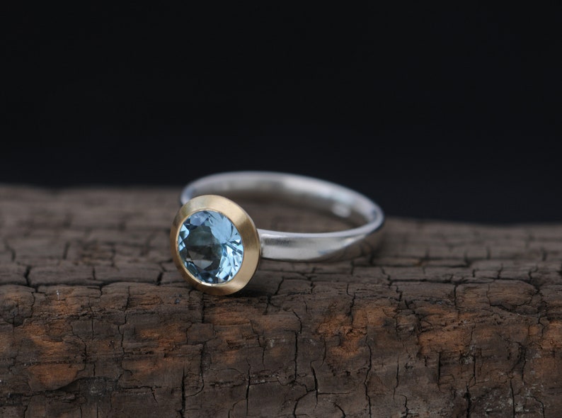 Puede incluir: Un anillo de plata con un engaste de oro con una piedra preciosa azul claro.