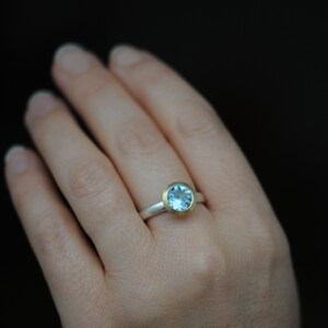 Puede incluir: Un anillo de plata con una banda de oro y una piedra preciosa azul claro.