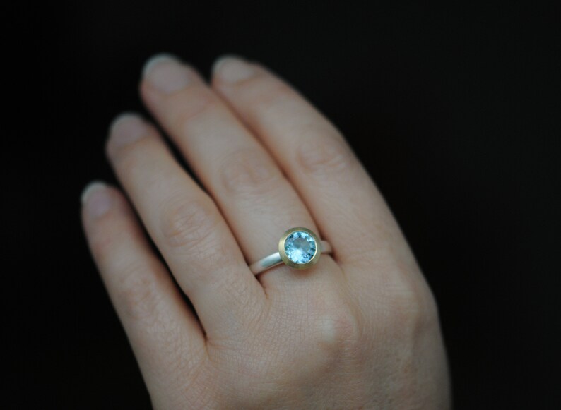 Puede incluir: Un anillo de plata con una banda de oro y una piedra preciosa azul claro.