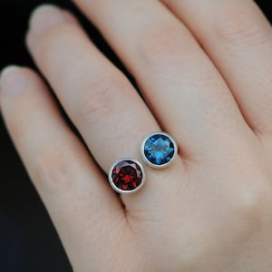 Peut inclure: Une bague en argent avec deux pierres rondes. La plus grande pierre est bleue et la plus petite est rouge.