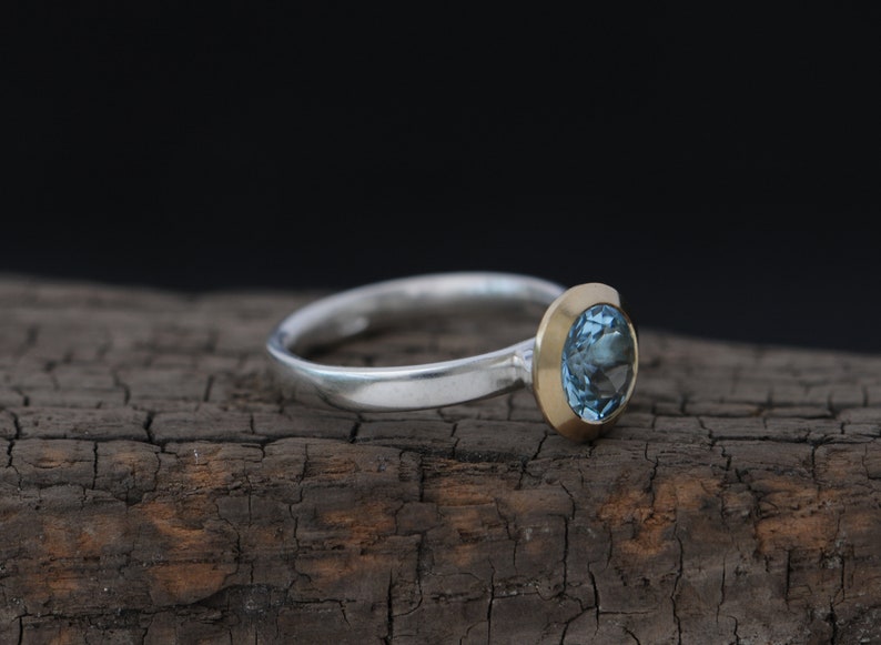 Puede incluir: Un anillo de plata con engaste de oro y una piedra preciosa azul.