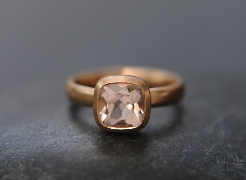 May include: A rose gold ring with a square-shaped, light pink gemstone.
